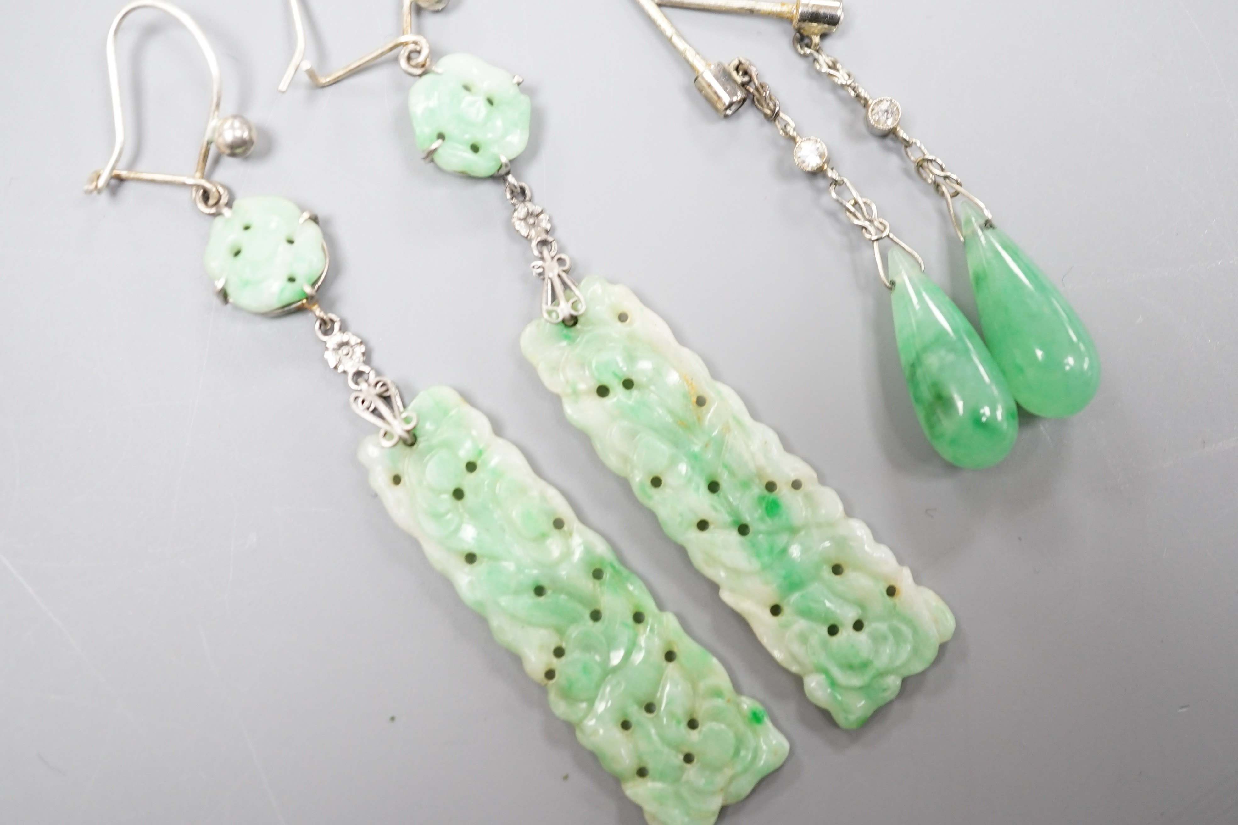 A pair of white metal pair shaped jade and two stone diamond set drop earrings, 37mm and one other pair of carved jade drop earrings, gross weight 8 grams.